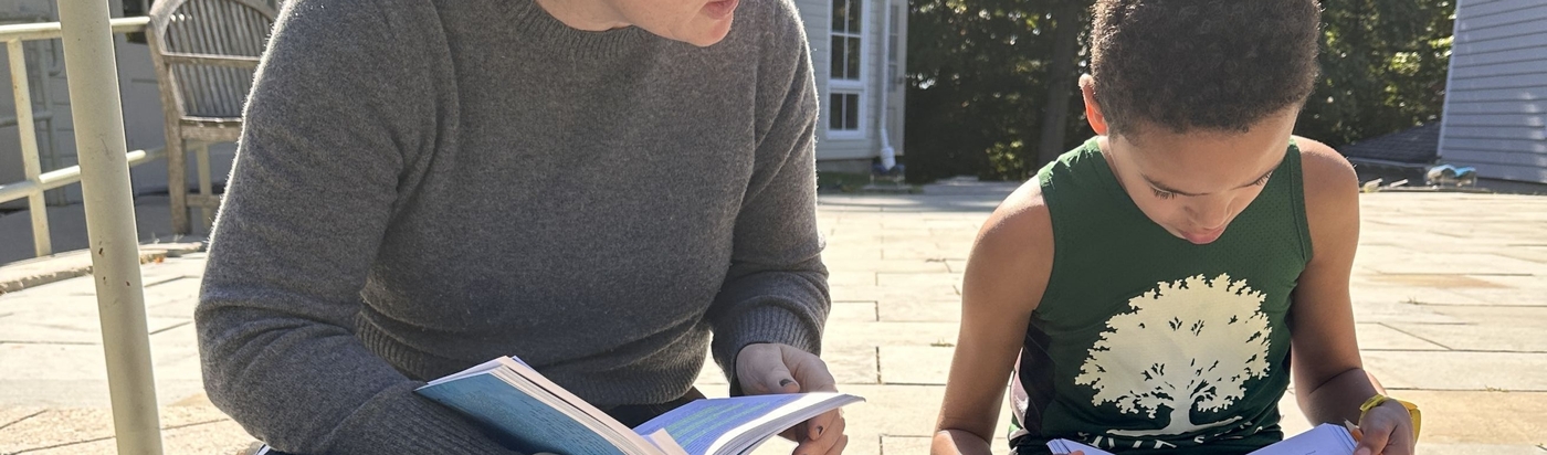 A teacher and student sit on the school steps reading together during all school reading time